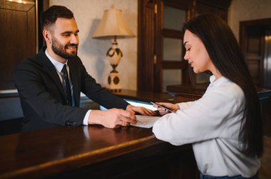 Otel resepsiyonisti kayıt işlemleri sırasında bayan bir konuğa yardım ediyor, mükemmel bir konukseverlik hizmeti sunuyor.
