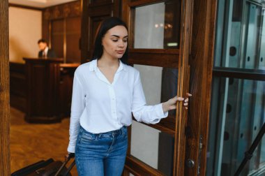 Bavullarıyla lüks bir otel lobisine giren ve resepsiyona giriş yapmaya hazırlanan bir kadın misafir.