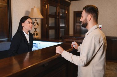 Gülümseyen resepsiyonist, konukseverlik hizmetleri sunan lüks bir otel lobisine giriş için erkek bir konuğa yardım ediyor.
