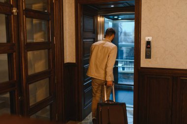 Seyahat valizli bir adam modern bir otel asansörüne biniyor, seyahatine hazırlanıyor ya da konakladıktan sonra ayrılıyor.