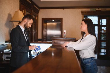 Resepsiyonist, takım elbiseli bir adama pasaportunu sunması için klasik bir otel lobisinde yardım ediyor.