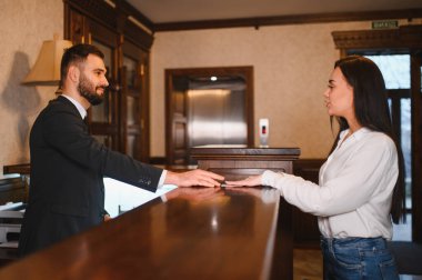Otel resepsiyonisti lüks bir lobide bayan bir konuğa yardım ediyor, müşteri hizmetlerini kontrol sırasında sağlıyor.