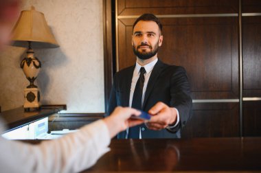 Otel resepsiyonisti lobi masasındaki bir müşteriye kredi kartı ödemesi yapıyor. Mükemmel bir konukseverlik ve hizmet sunuyor.