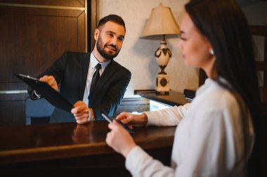 Otel resepsiyonisti lobi masasına giriş yaparken kayıt için kadın bir konuğa pano veriyor.