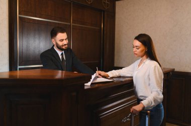 Resepsiyon masasında evrakları imzalayan kadın bir gezgin, çeke yardım eden bir erkek otel çalışanı. Konukseverlik servisi