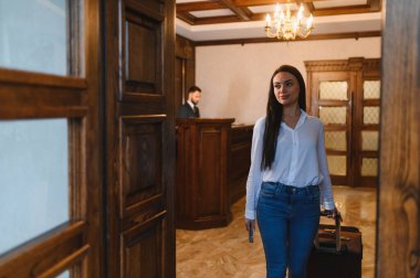 Otele gelen bir kadın zarif lobiden bir bavul geçiriyordu. Resepsiyonist arka planda resepsiyonda çalışıyor.