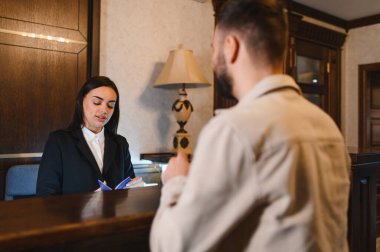 Otelin lobi masasında duran bir müşteri hizmetleri görevlisi ile konuşan bir bayan.