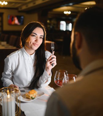 Bir kadın çatal tutuyor, gülümsüyor ve zarif bir restoranda romantik bir akşam yemeğinde partnerine bakıyor.