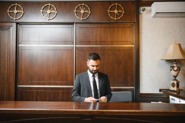 Lüks bir otel lobisinde resepsiyonist olarak çalışan genç bir işadamı. Bir kartın detaylarını kontrol ediyor.