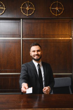 Masanın arkasında duran arkadaş canlısı resepsiyonist lüks bir oteldeki karşılama servisi için konuğa anahtar kartı sunuyor.