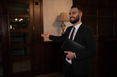 Siyah takım elbiseli otel çalışanı hoş geldin jesti yapıyor, misafirler için misafirperver bir ortam yaratıyor.