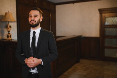 Lüks bir otel lobisinde resepsiyonda duran gülümseyen profesyonel bir adam mükemmel bir konukseverlik hizmeti sunuyor.