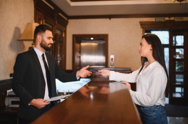 Otel çalışanı, resepsiyondaki gülümseyen bir bayana anahtar kartı veriyor. Hizmette hızlı ve etkili bir kontrol sağlıyor.
