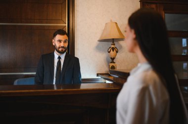 Takım elbiseli otel kapıcısı zarif resepsiyon masasında konukseverlik hizmeti veriyor.