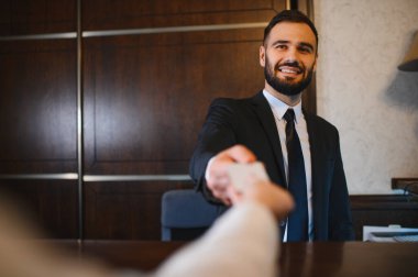 Otel resepsiyonisti gülümsüyor, çekmecedeki bir konuğa anahtar kartı veriyor, mükemmel bir konukseverlik hizmeti sunuyor.