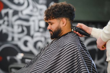 Berber dükkanında saç kesiciyle saç kestirip berberden yeni çıkmış bir adam. Erkek bakımına ve tarzına odaklan