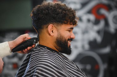 Kıvırcık saçlı ve sakallı bir adam berberden yeni bir soluk saç kesimi alıyor.