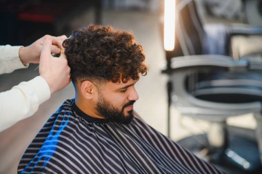 Berber dükkanı müşterisi yeni bir saç tıraşı oluyor, berber elleri kıvırcık saçlarını modern bir saç stili için şekillendiriyor.