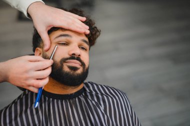 Profesyonel sakal alan adam berberden düzgün bir jilet kullanarak stil ve hassasiyete odaklanıyor.