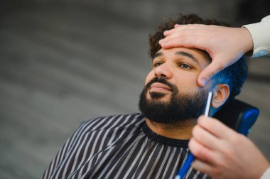 Profesyonel berber dükkanında berber tarafından tıraş edilip sakal tıraşı olan bir adam.