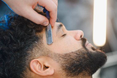 Berber dükkanında sakal tıraşı olan bir adam, sakalını temiz ve şık bir görünüme odaklıyor.