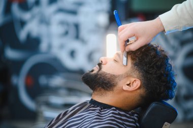 Berberler, modern bir berber dükkanında düzgün bir jiletle müşterinin sakalını şekillendiriyor.