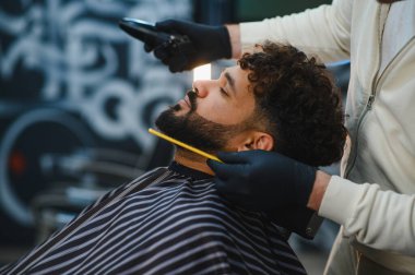 Sakallı adam modern bir berber dükkanında profesyonel sakal kesimi ve stil alıyor.