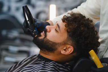 Modern, şık bir berber salonundaki bir berberden saç kesimi ve sakal kesimi yaptıran adam.