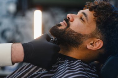 Adam sakalını elektrikli makasla ustalıkla şekillendirirken rahatlıyor. Tımar ve şekillendirme Modern bir yüz kılı görünümü