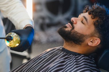 Berber koltuğunda dinlenen adam sakalı ve derisi için şımartıcı bir tıraş spreyi tedavisi görüyor.