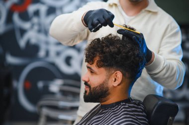 Profesyonel berber kesimi ve stili modern berber dükkanında genç adamın kıvırcık saçı ve sakalı, titiz tımar ve yeni moda.