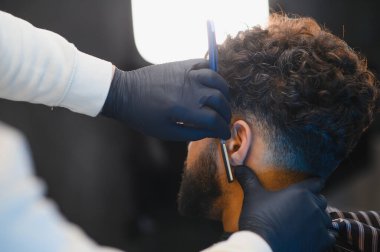 Berber, bir adamın boynu ve favorisi boyunca tıraş etmek için düz bir jilet kullanır, tımar ve stil üzerine odaklanır.