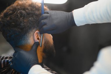 Profesyonel berber bir tıraş seansı sırasında keskin bir usturayla bir adamın boynunu dikkatlice tıraş ediyor.