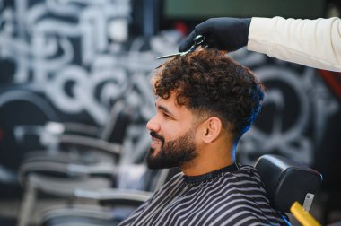 Kıvırcık saçlı bir adam berberden profesyonel bir saç kesimi alıyor, mutlu hissediyor ve şık bir bakım deneyimi arıyor.