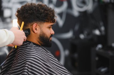 El kamerası makasları sakallı ve kıvırcık saçlı bir adamın saçını buduyor, berber dükkanından taze bir kesim alıyor.