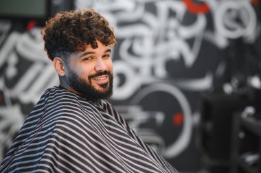 Taze tıraşlı, berber dükkanında sakallı, kendine güvenen, şık görünümlü, kameraya bakan, modern kuaför portresi olan gülümseyen adam.