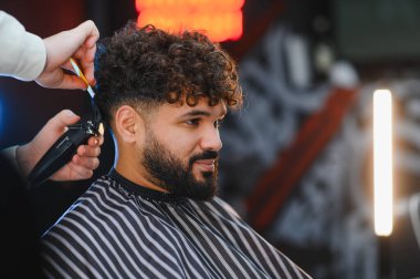 Saç makası ve tarak kullanarak berberden yeni saç tıraşı olan bir adam. Tımar ve modern saç stiline odaklan.