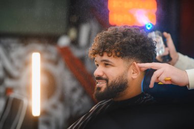 Gülümseyen müşteri, modern bir berber dükkanında saç bakımını ve bakımını gösteren yeni bir saç stili alıyor.