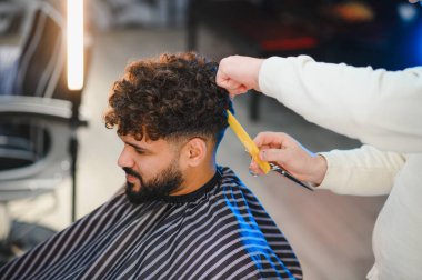 Modern berber dükkanındaki erkek müşterinin kıvırcık saçlarını berber stili, profesyonel tımar ve yeni moda saç kesimi.