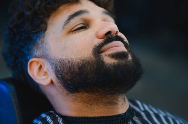 Müşteri, modern bir berber dükkanında özet oluşturup şekillendirme yaparken profesyonel sakal gevşetiyor.