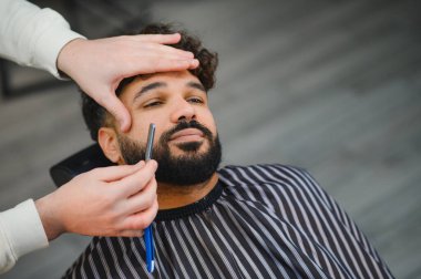 Modern berber dükkanında ustaca şekillendirilen ve tımar edilen profesyonel sakallı bir adam.