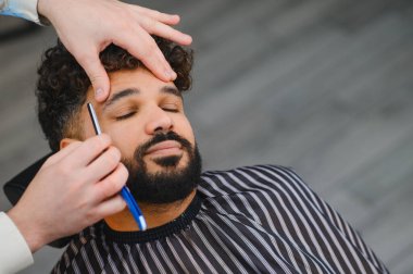 Berber, müşterinin sakalını ve bıyığını ustura ile şekillendiriyor. Temiz, profesyonel bir tımar deneyimi için.