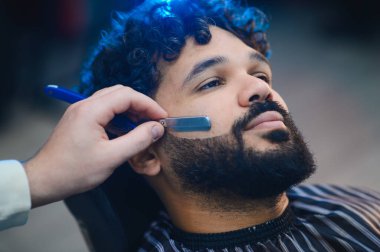 Bir müşterinin sakalını jiletle kesmek profesyonel bir berber dükkanında temiz ve kusursuz bir kenar sağlamak.