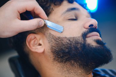 Profesyonel bir berber dükkanında düzgün bir sakal çizgisi yaratmak için berberden tıraş olan bir adam.