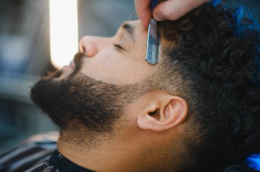 Bir berber dükkanında profesyonel sakal ve saç kesimi yaptıran bir adam, erkek stili için geleneksel tımar deneyimini yaşıyor.