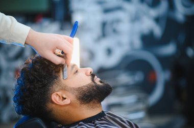 Erkek berber, berber dükkanında jiletle tıraş olan bir erkeğe profesyonel sakal tıraşı ve sakal kesimi yapıyor.