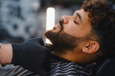 Profesyonel berber bir adamın sakalını dikkatlice kesiyor, şık bir bakım ve rahatlatıcı bir güzellik salonu deneyimi sağlıyor.