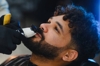 Berber, bir müşterinin sakalını ve bıyığını elektrikli jiletle dikkatlice buduyor.