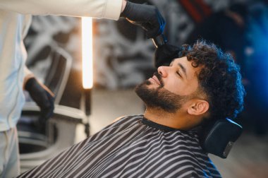 Berber, modern berber dükkanında saç kesimi üstüne saç fırçasıyla müşterinin boynundaki gevşek saçların tozunu alıyor.