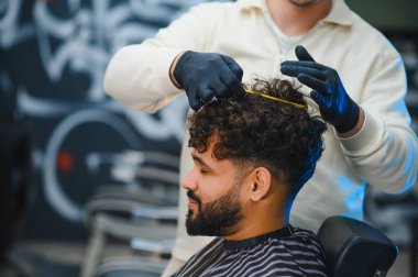 Modern bir berber dükkanında, erkek müşterinin zengin, siyah kıvırcık saçlarını taramak için bir tarak ve eller kullanan profesyonel berber.